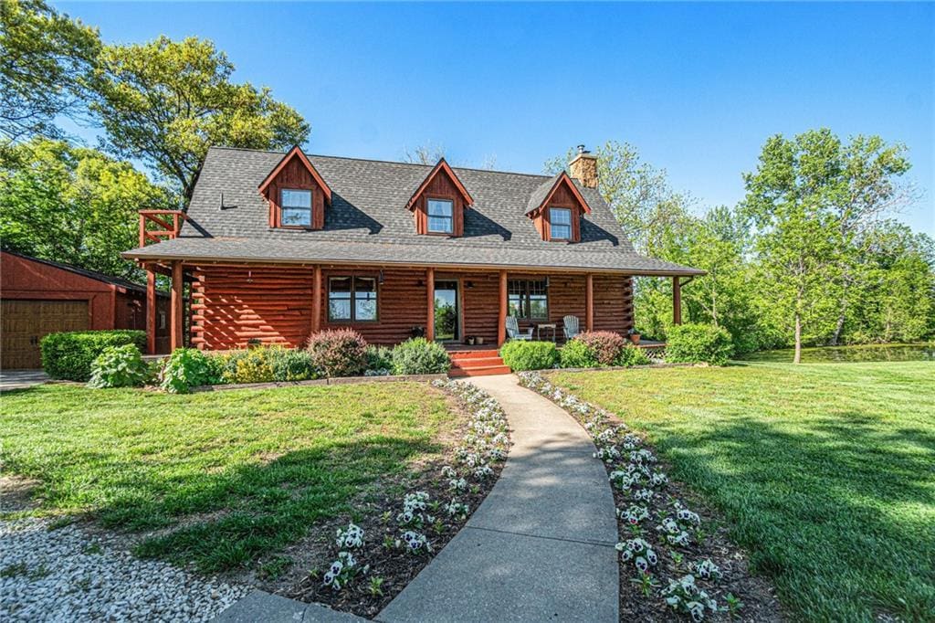 1457 Haskell Rd, Williamsburg, KS 66095 - cabin with covered porch, a chimney, log siding, and a front lawn
