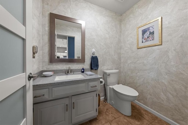 half bathroom featuring baseboards, vanity, tile patterned flooring, and toilet