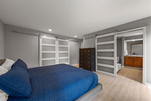 bedroom with wood finished floors, visible vents, recessed lighting, and a barn door