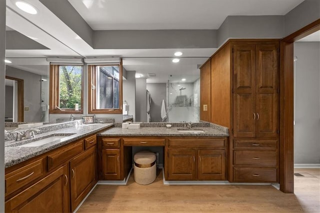 full bath with double vanity, walk in shower, wood finished floors, and a sink