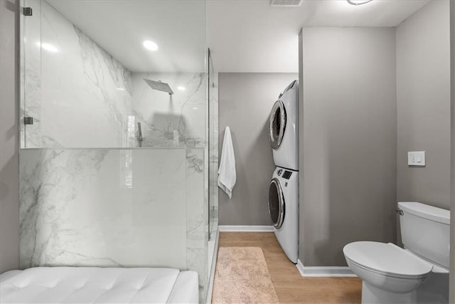 bathroom featuring stacked washer and dryer, wood finished floors, a marble finish shower, and toilet
