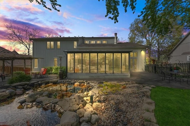 back of house at dusk featuring fence, a sunroom, and a patio