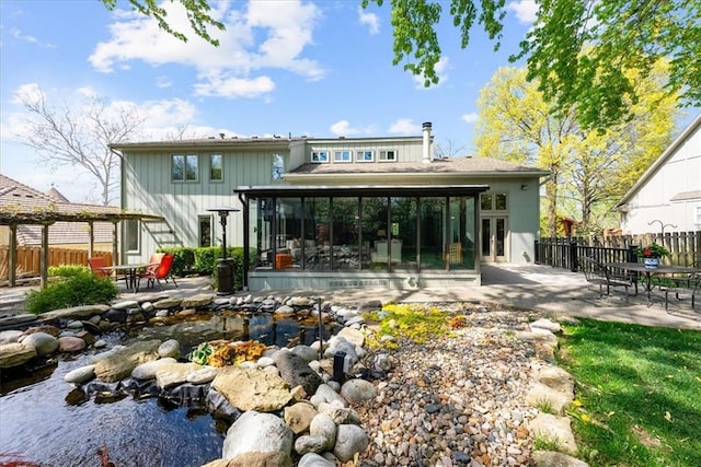 rear view of house with a sunroom, fence, a patio, and a garden pond