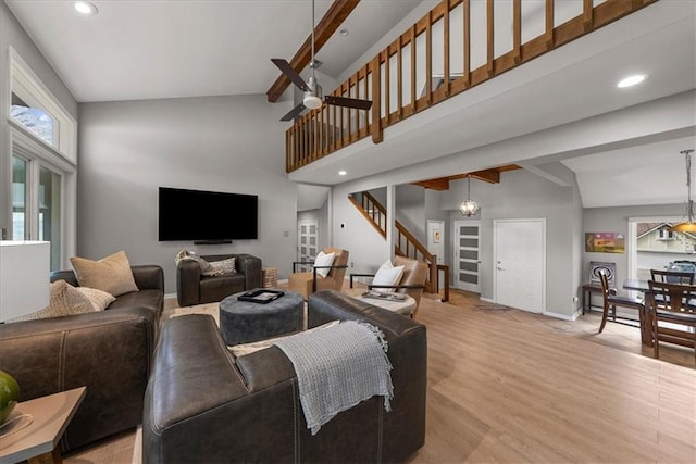 living room featuring baseboards, a towering ceiling, light wood-style floors, a ceiling fan, and stairs