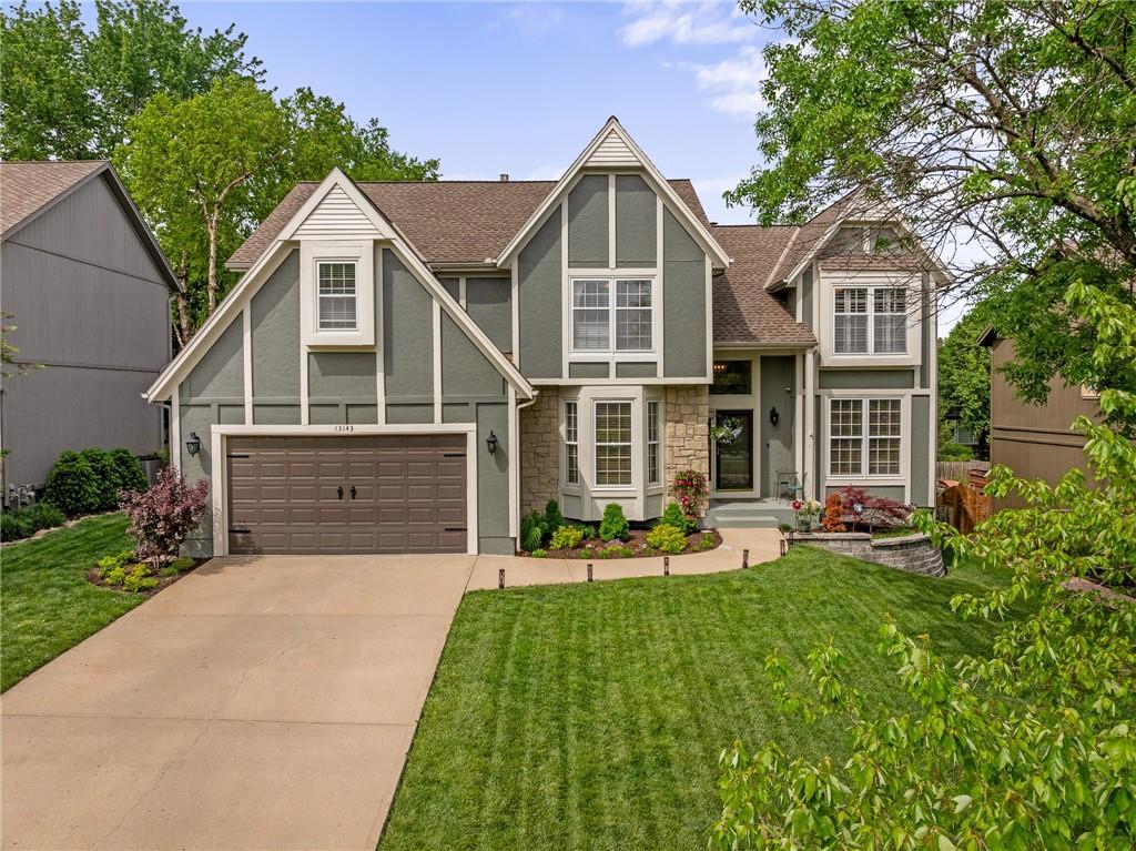 tudor home featuring a shingled roof, stone siding, stucco siding, a front yard, and driveway