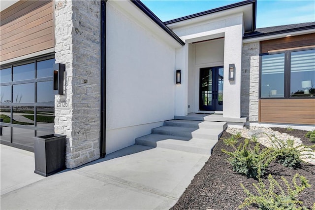 entrance to property with french doors, stone siding, a garage, and stucco siding