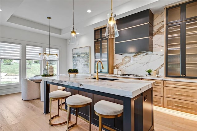 kitchen with a raised ceiling, white gas cooktop, light wood-style floors, decorative backsplash, and a sink