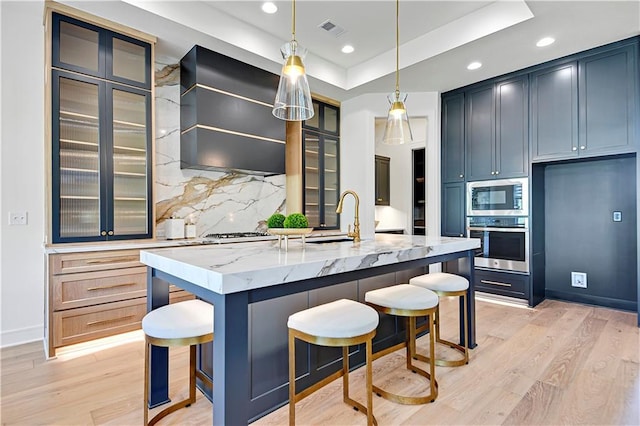 kitchen with custom exhaust hood, visible vents, appliances with stainless steel finishes, a tray ceiling, and light stone counters