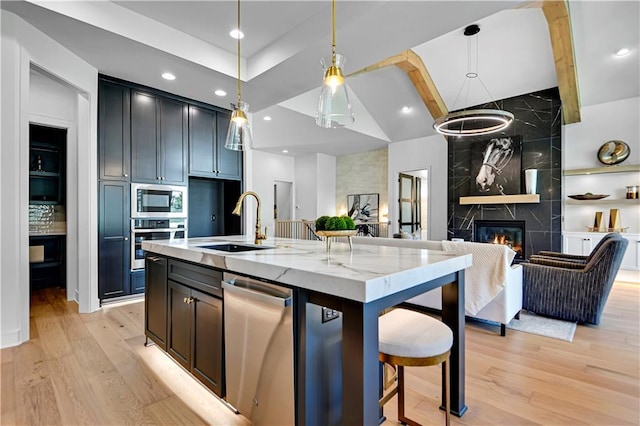 kitchen featuring open floor plan, a high end fireplace, light wood finished floors, light stone countertops, and stainless steel appliances