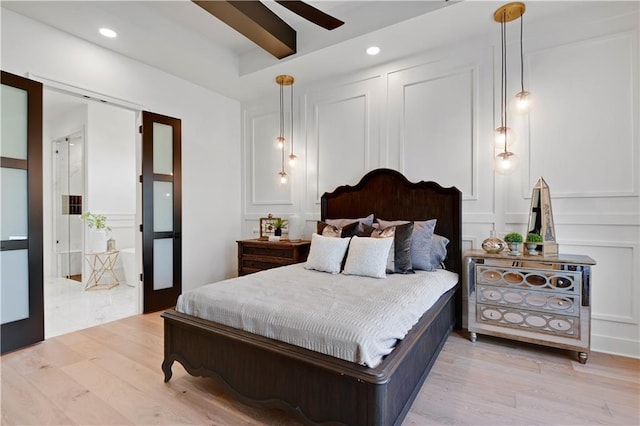 bedroom featuring a decorative wall, beam ceiling, recessed lighting, and light wood-style floors