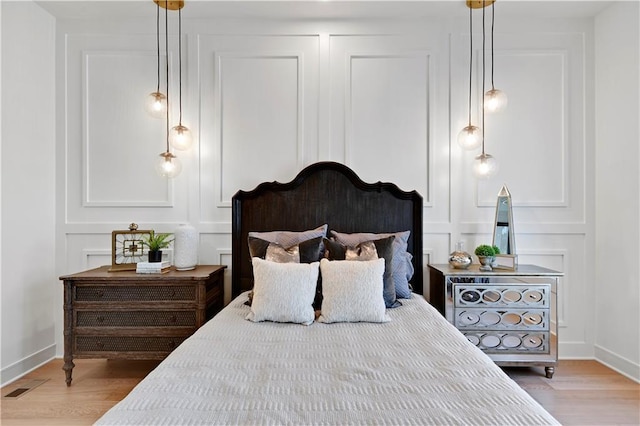 bedroom with light wood-type flooring, a decorative wall, baseboards, and visible vents