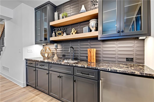 bar featuring refrigerator, light wood-style floors, visible vents, decorative backsplash, and a sink