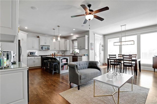 living area featuring plenty of natural light, dark wood finished floors, and ceiling fan with notable chandelier