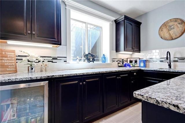kitchen featuring wine cooler, light stone counters, backsplash, and a sink