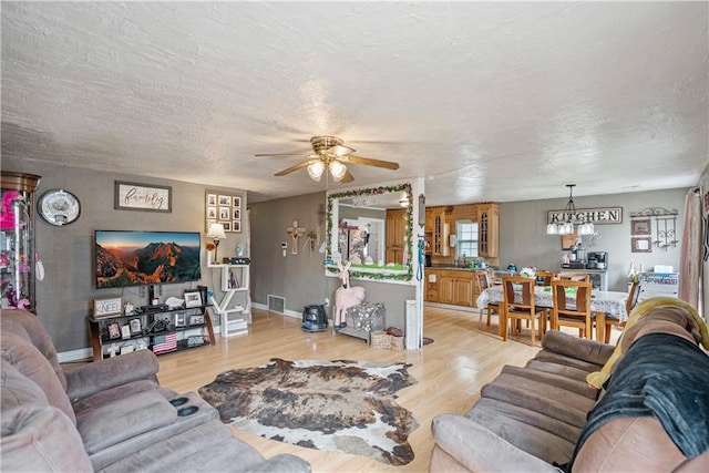 living area featuring a textured ceiling, visible vents, baseboards, wood finished floors, and ceiling fan with notable chandelier