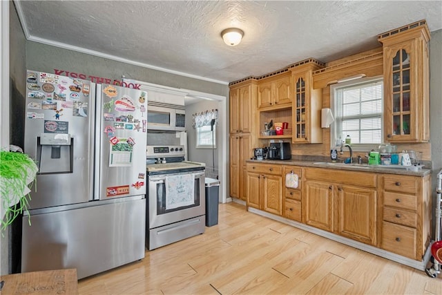 kitchen featuring a textured ceiling, light wood-style flooring, stainless steel appliances, glass insert cabinets, and a sink