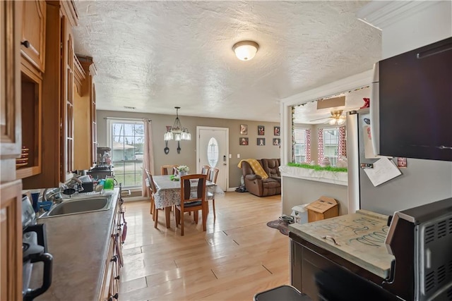 kitchen with a textured ceiling, hanging light fixtures, a sink, light wood finished floors, and brown cabinetry