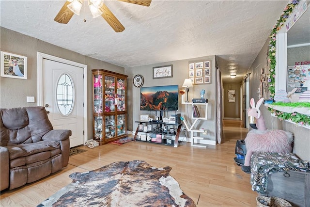 living room featuring a textured ceiling, baseboards, ceiling fan, wood finished floors, and a textured wall