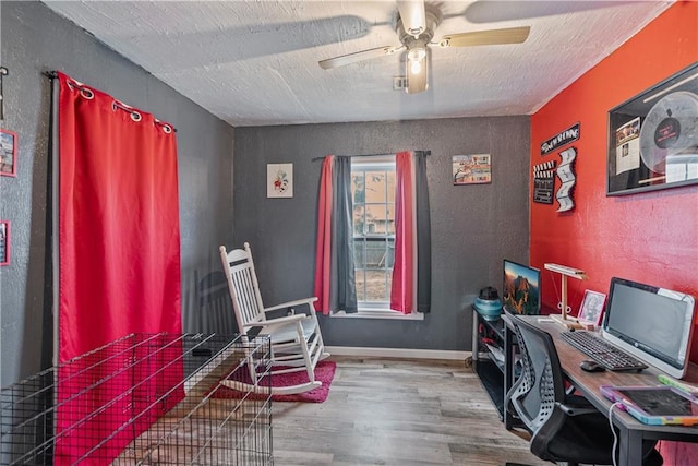 home office with wood finished floors, a textured ceiling, baseboards, ceiling fan, and a textured wall