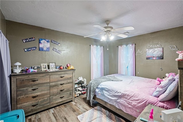 bedroom featuring a textured wall, visible vents, ceiling fan, and wood finished floors