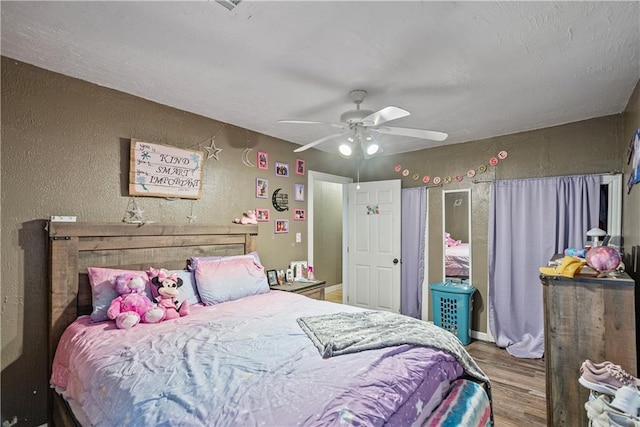 bedroom with a ceiling fan, a textured wall, and wood finished floors