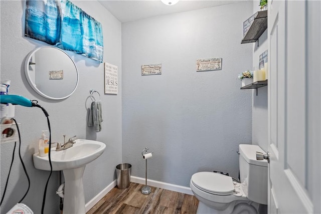 half bathroom featuring baseboards, wood finished floors, and toilet