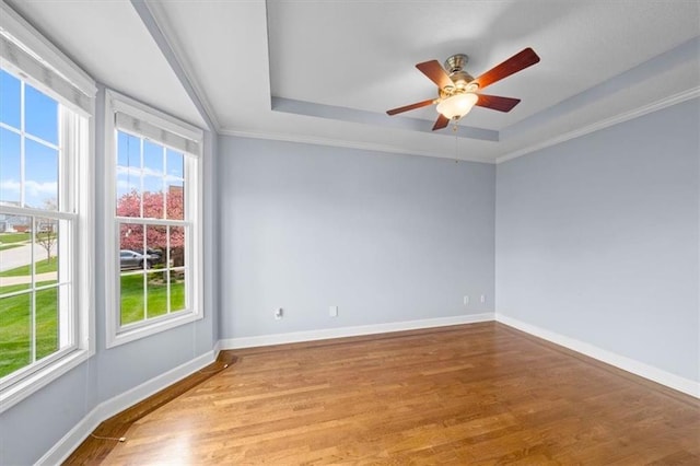 unfurnished room with ornamental molding, wood finished floors, baseboards, a raised ceiling, and a ceiling fan