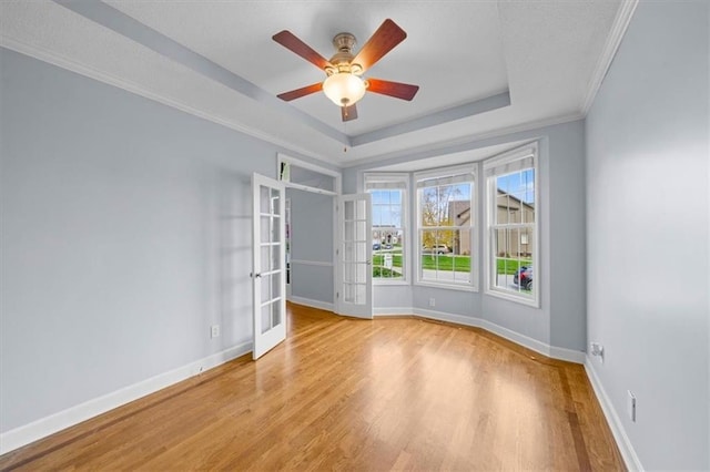 spare room with ceiling fan, french doors, wood finished floors, baseboards, and a tray ceiling