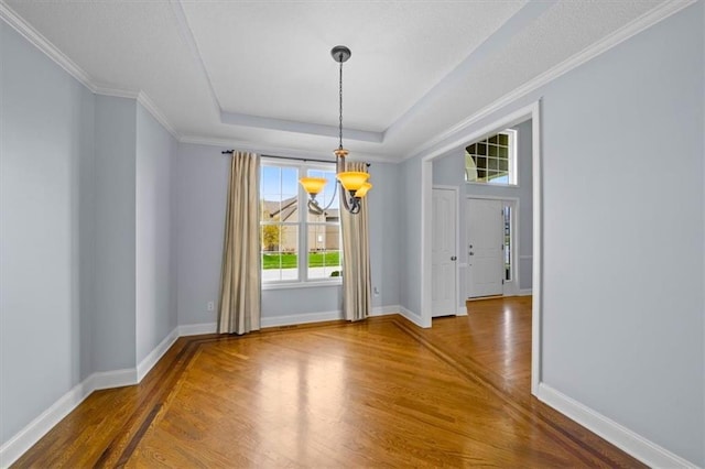unfurnished dining area featuring baseboards, a tray ceiling, an inviting chandelier, and wood finished floors