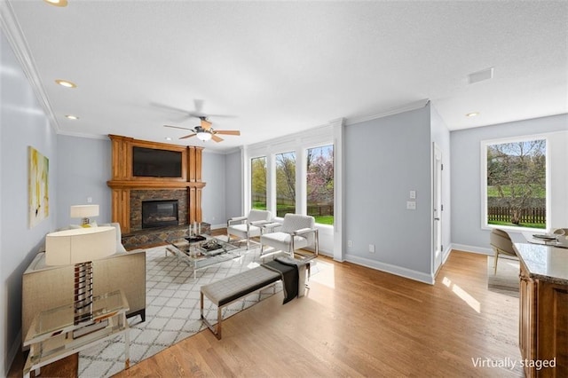 living room with light wood finished floors, a fireplace, a ceiling fan, baseboards, and ornamental molding