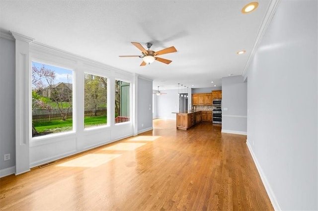 unfurnished living room with a ceiling fan, visible vents, baseboards, light wood finished floors, and ornamental molding