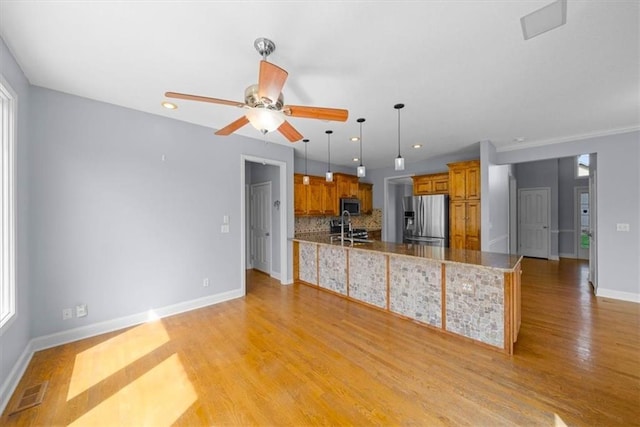 kitchen featuring appliances with stainless steel finishes, a sink, brown cabinetry, a peninsula, and baseboards