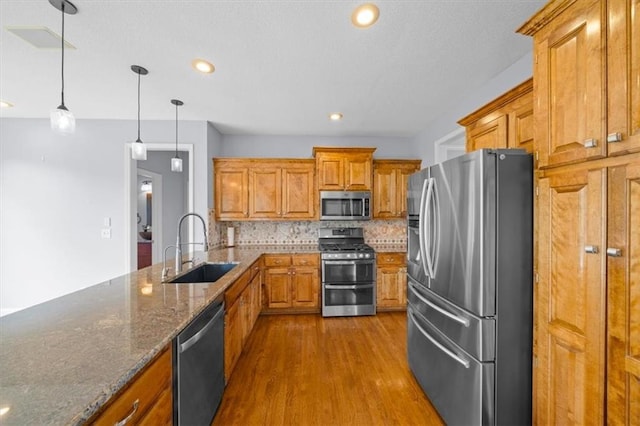 kitchen with dark wood-type flooring, brown cabinets, a sink, backsplash, and stainless steel appliances