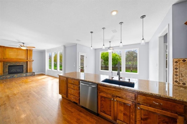 kitchen with a ceiling fan, a fireplace, brown cabinets, dishwasher, and a sink