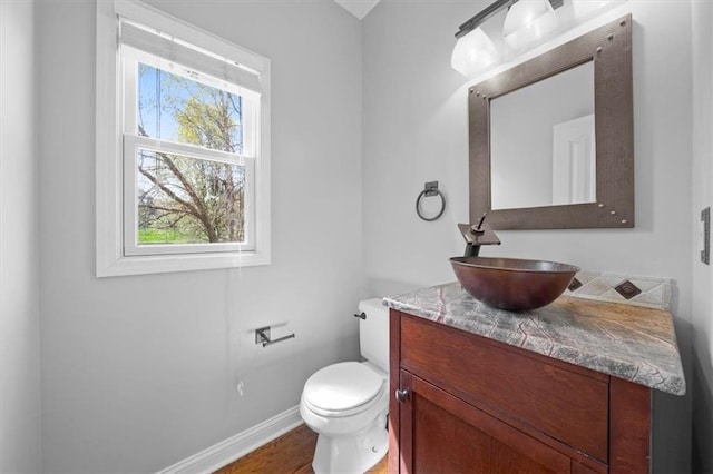 bathroom featuring baseboards, wood finished floors, toilet, and vanity