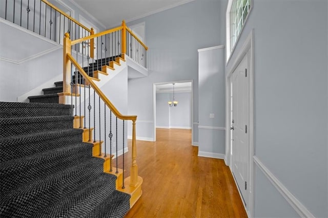 interior space featuring baseboards, wood finished floors, a towering ceiling, ornamental molding, and stairway