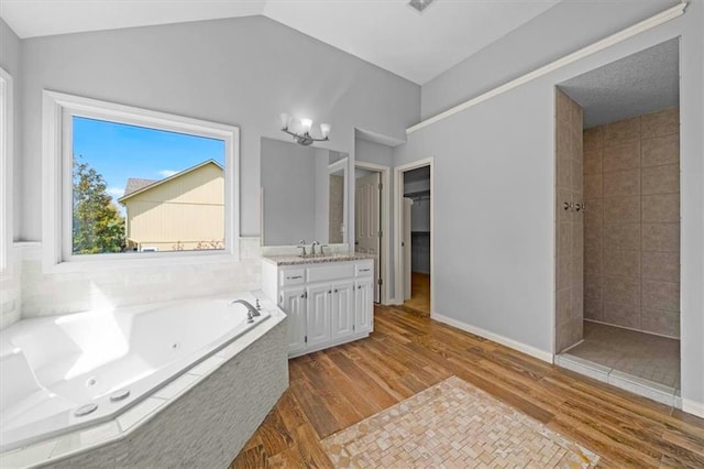 bathroom featuring vanity, a tub with jets, wood finished floors, vaulted ceiling, and tiled shower