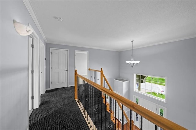 corridor with dark colored carpet, crown molding, a chandelier, and an upstairs landing