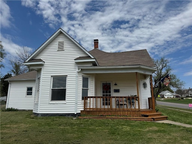back of property with a chimney, a porch, a yard, and a shingled roof