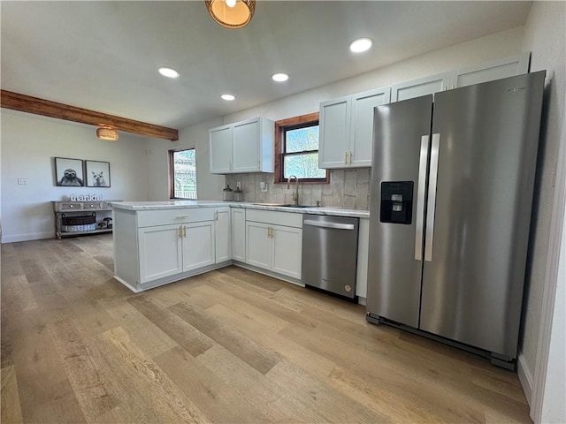 kitchen featuring a peninsula, appliances with stainless steel finishes, a sink, and light wood-style flooring