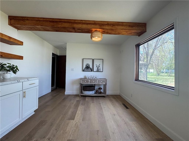 dining area with light wood-type flooring, baseboards, visible vents, and beamed ceiling