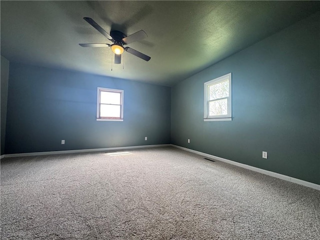 carpeted empty room with ceiling fan, baseboards, a healthy amount of sunlight, and visible vents