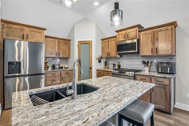 900 NW Lindenwood Dr, Grain Valley, MO 64029 - kitchen with appliances with stainless steel finishes, brown cabinetry, light wood-style floors, a sink, and lofted ceiling