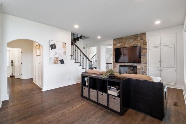 living area with stairway, arched walkways, baseboards, and dark wood-style floors