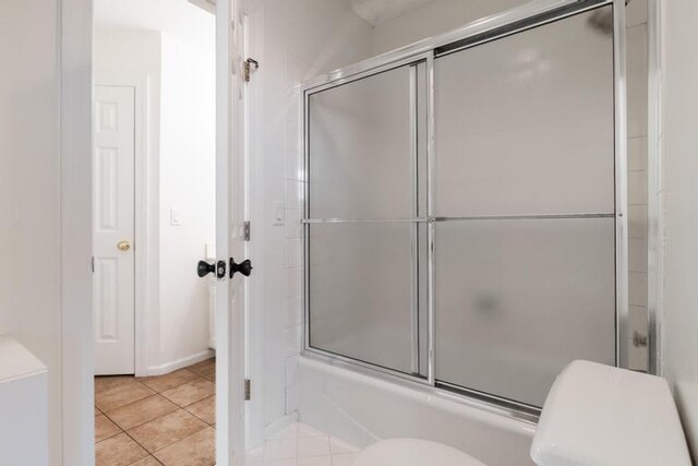 full bath featuring toilet, tile patterned floors, and combined bath / shower with glass door
