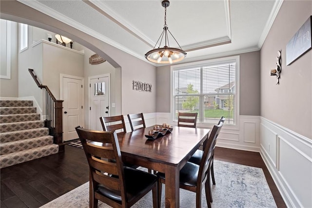 dining space with dark wood-style flooring, arched walkways, a wainscoted wall, a raised ceiling, and an inviting chandelier