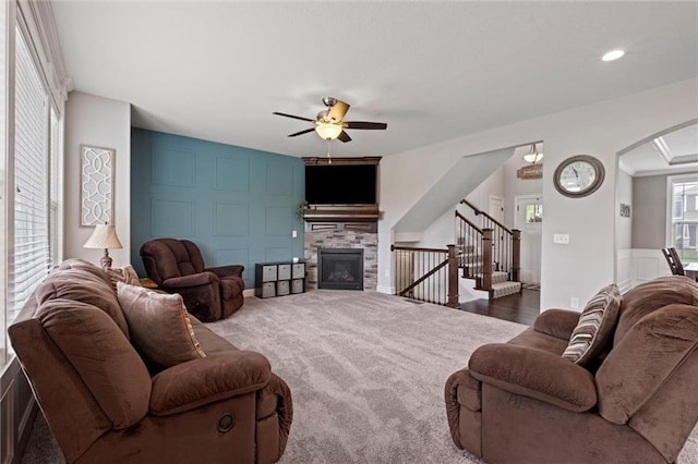 carpeted living room with a ceiling fan, arched walkways, a fireplace, and stairway