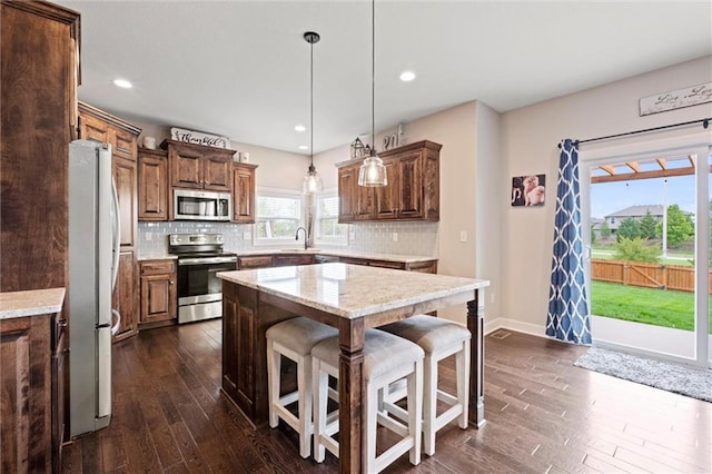 kitchen featuring dark wood-style floors, a kitchen bar, a center island, appliances with stainless steel finishes, and backsplash