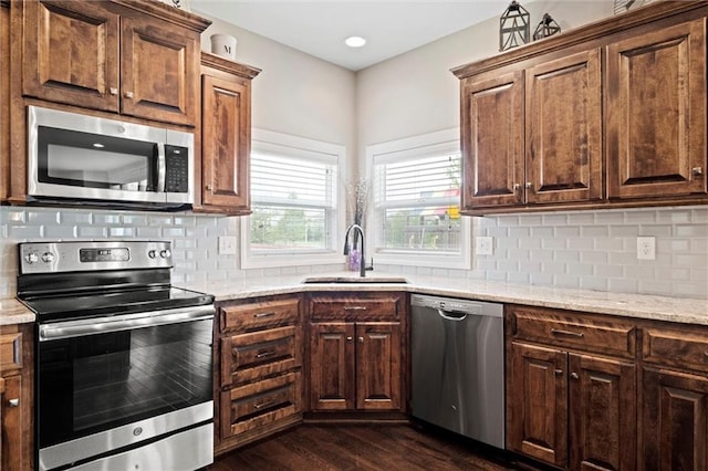 kitchen featuring dark wood-style flooring, light stone countertops, a sink, stainless steel appliances, and decorative backsplash
