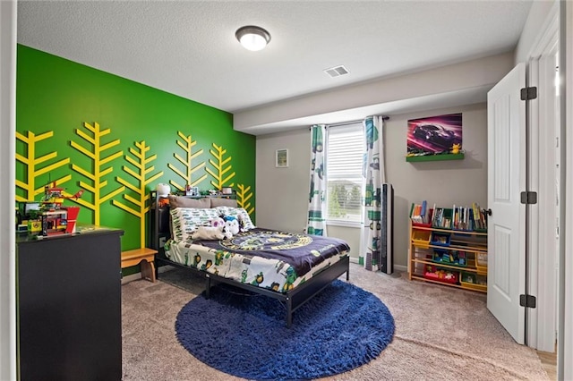 carpeted bedroom with baseboards, an accent wall, a textured ceiling, and visible vents